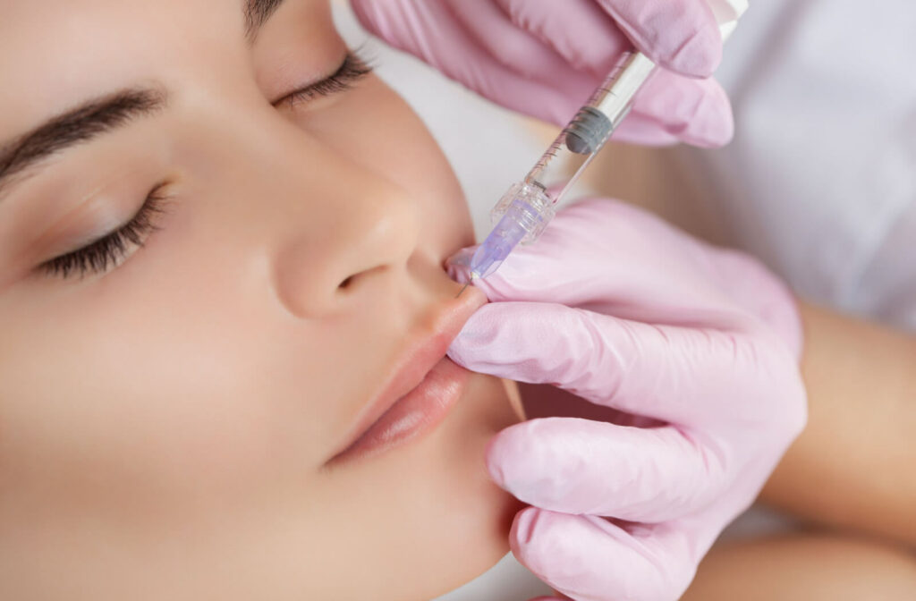 The cosmetologist making a lip augmentation procedure on a woman.